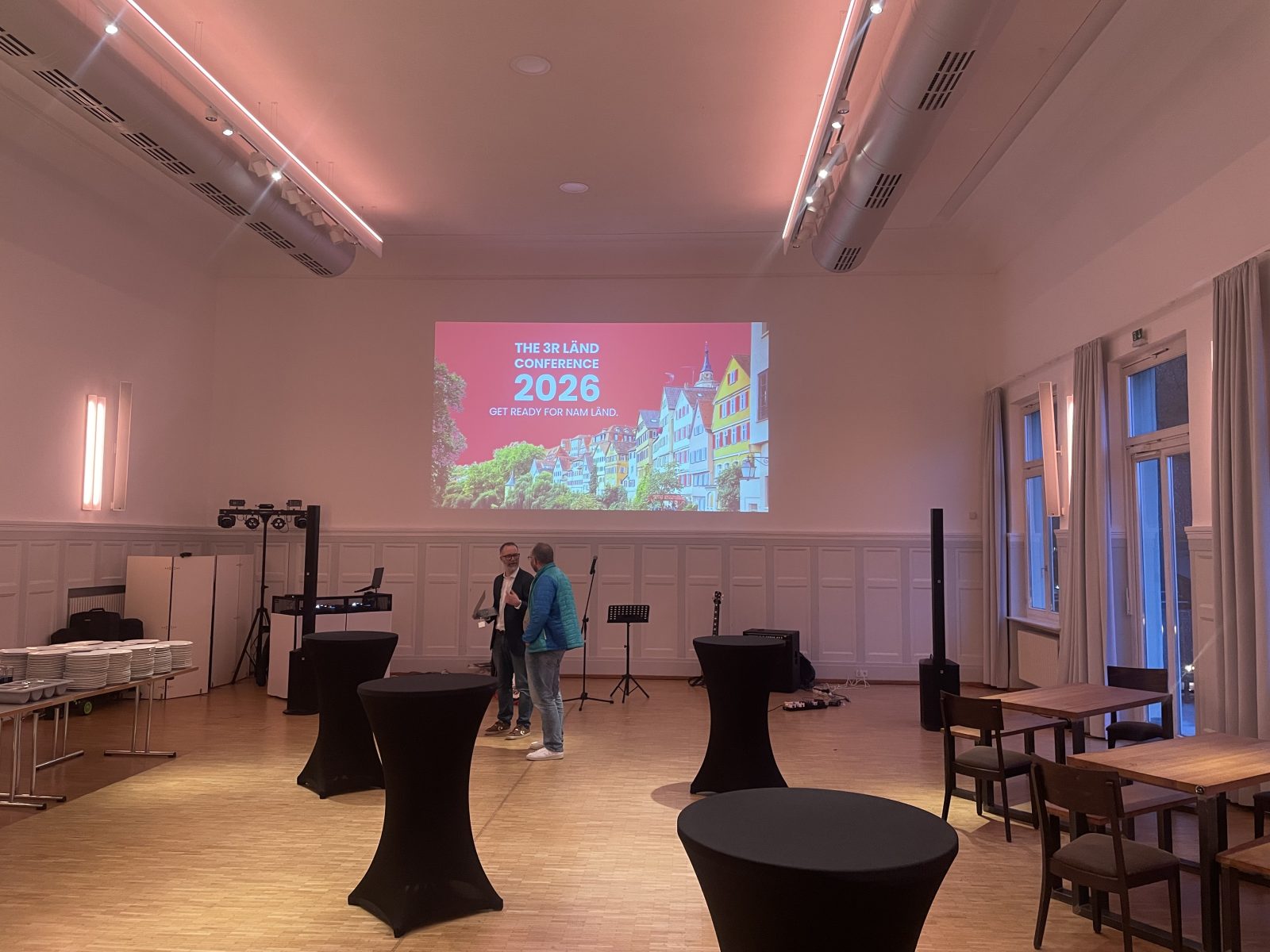 Veranstaltungssaal mit Leinwand, Stehtischen und Beschallung